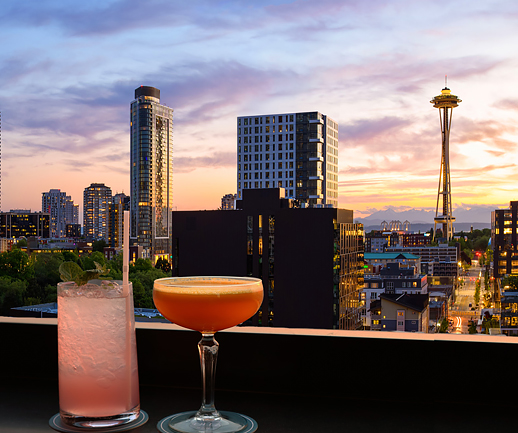 two cocktails on a table with the city on the background