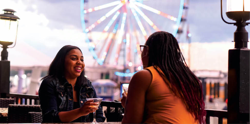 two friends drinking cocktails with a ferris wheel in the background