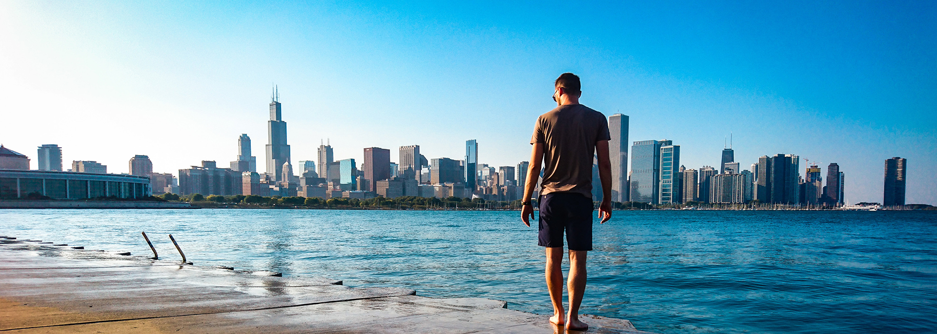 man walking along edge of water with chicago skyline in view