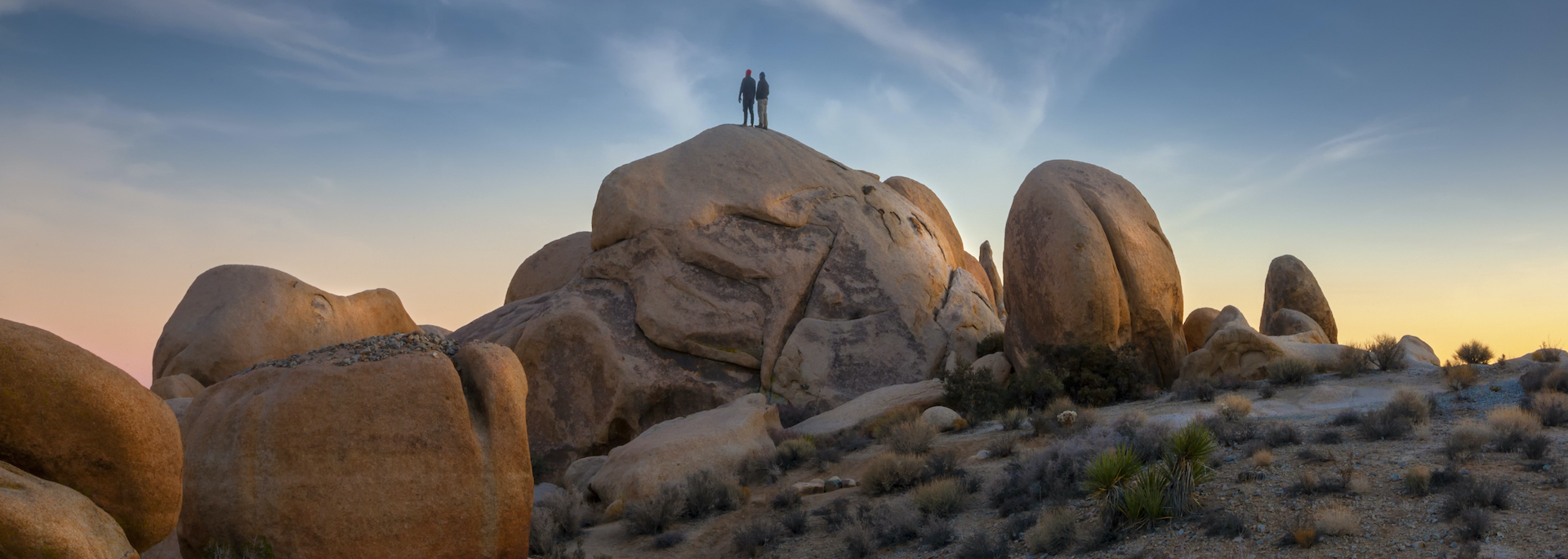 two people standing on top of a rock in the desert