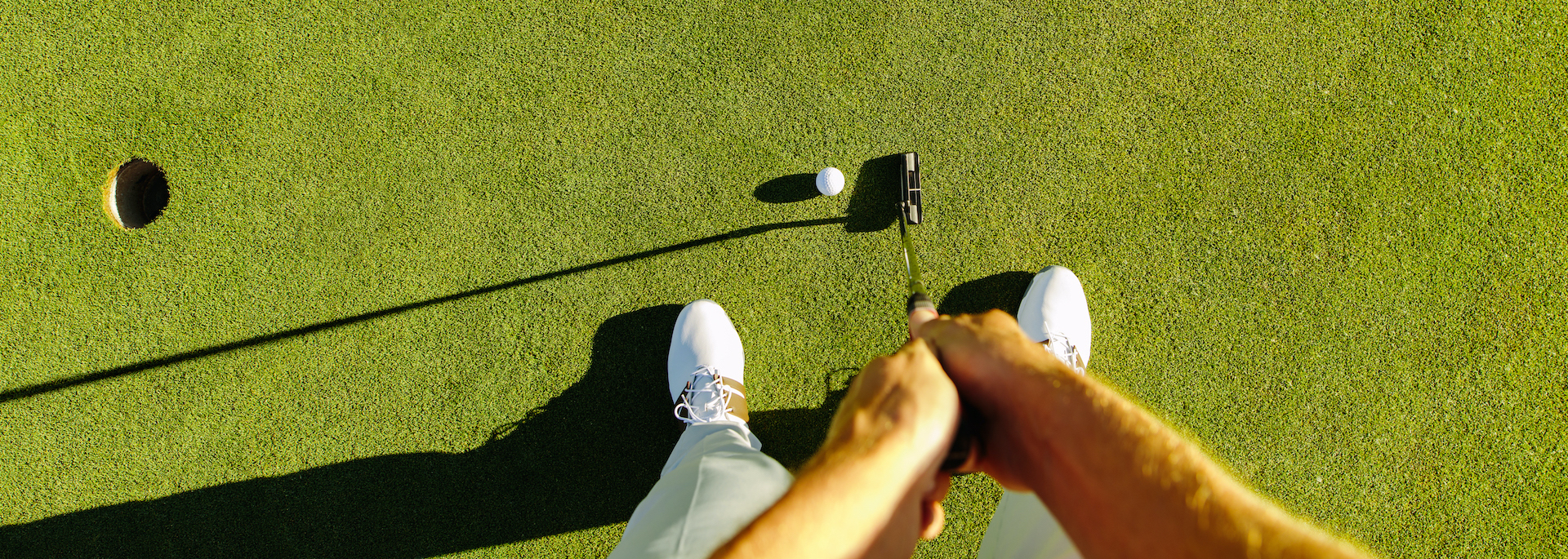 person with two hands on golf club lining up to hit a white golf ball