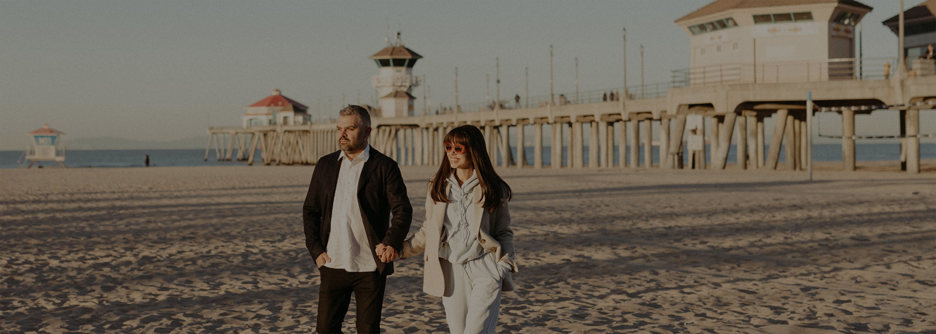 couple holding hands walking in front of fishing pier