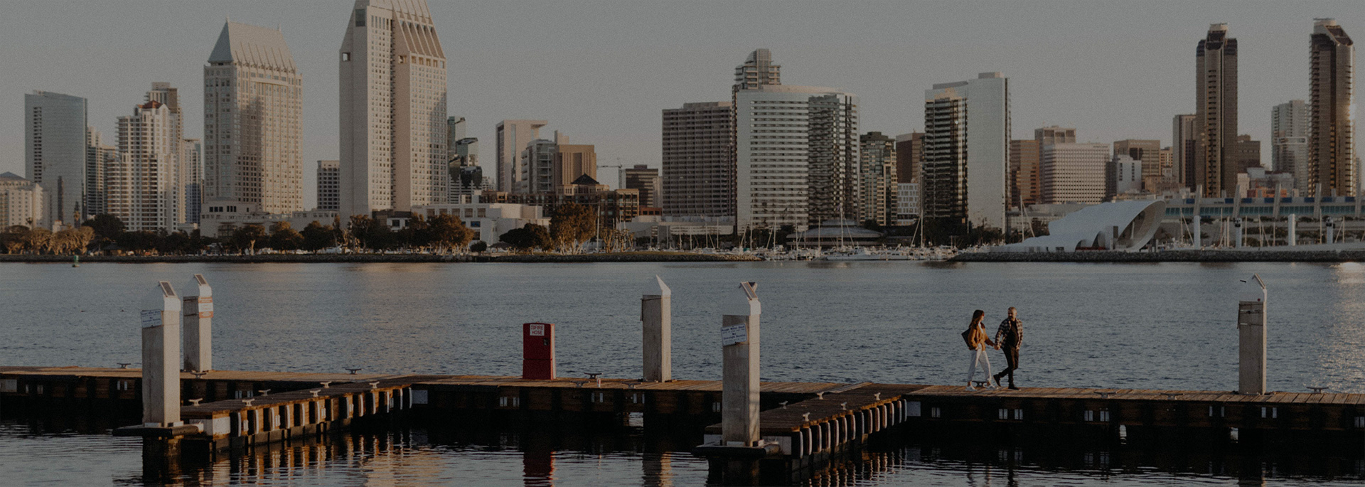 couple holding hands and walking on dock with view of downtown san diego