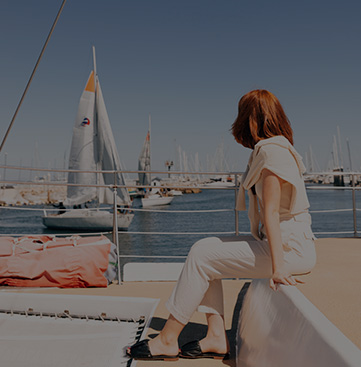 woman sitting on boat looking out at water with other sailboats floating by