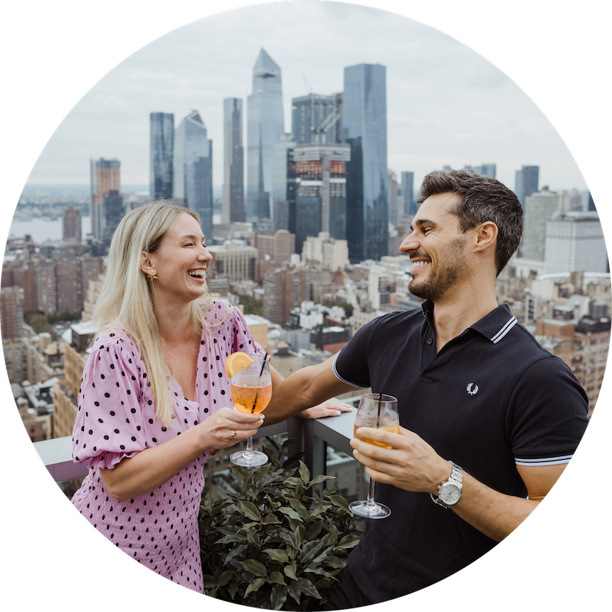 couple smiling at one another and cheerings cocktails on rooftop overlooking new york city