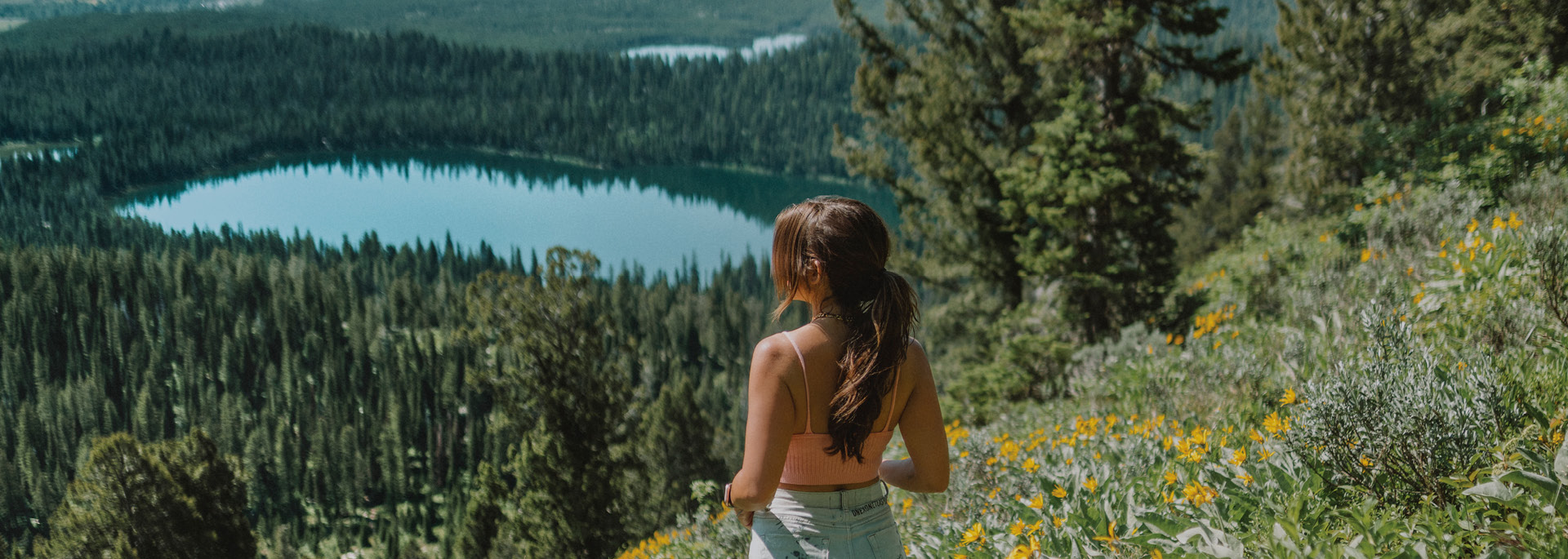 woman at a top of a mountain looking down at trees and a lake