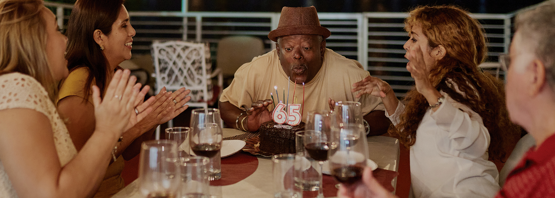 man blowing out birthday candles while friends sing happy birthday