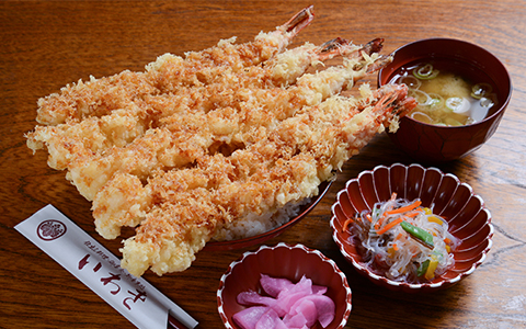 Five large pieces of shrimp tempura served on a rice bowl with side dishes and miso soup