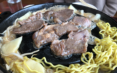 slices of lamb cooking on a steel plate with noodles