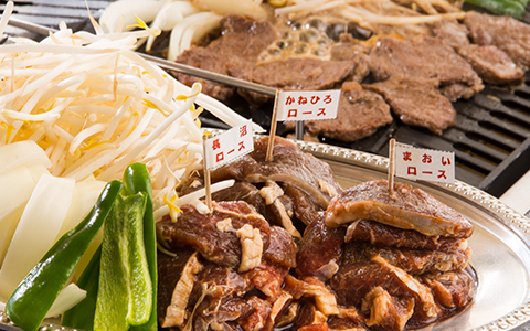 Slices of lamb cooking on the grill with a side dish of vegetables