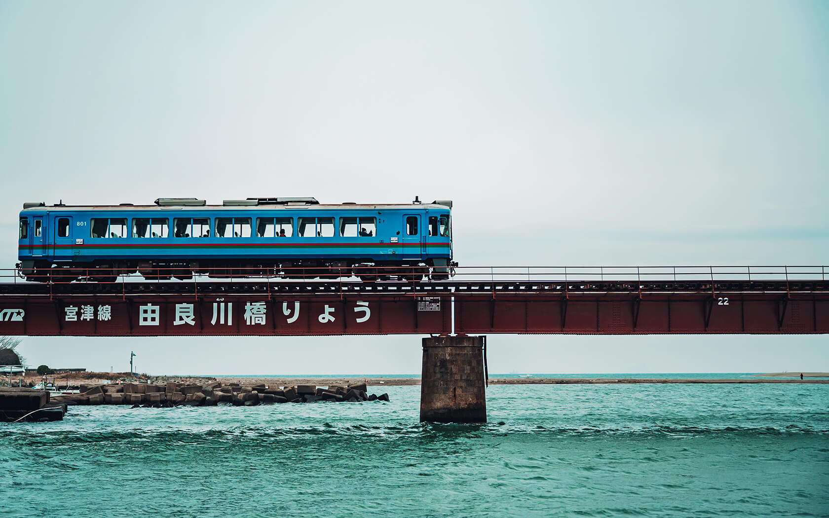 a blue train passing on a train track that is over the water
