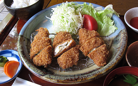 A plate of deep-fried pork cutlets with vegetables and rice on the side