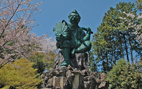 A large statue of a Tengu (long-nosed goblin) standing between the trees.