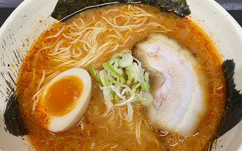 A bowl of ramen noodles with slice pork and a boiled egg on top