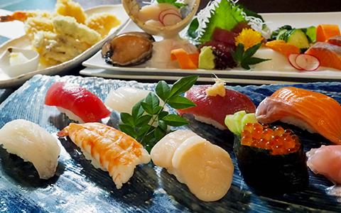 A plate with several types of sushi and a plate of sashimi in the back