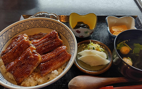 A bowl of grilled eel and rice with soup and pickles