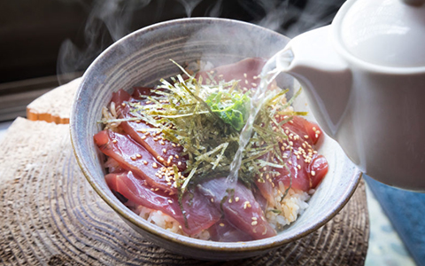 Hot tea being poured over a bowl of rice and fresh fish