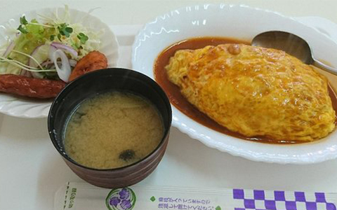 A plate of omelette with rice, salad, and miso soup