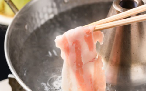 A slice of pork being placed into a hot pot