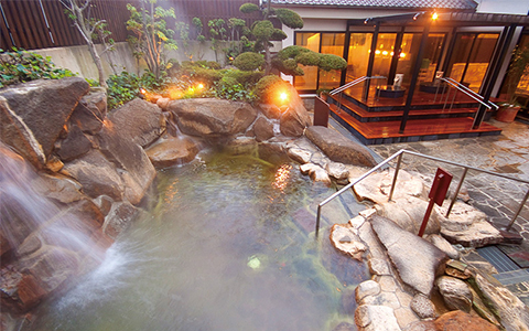 View of an outdoor onsen hot spring with an indoor facility in the background