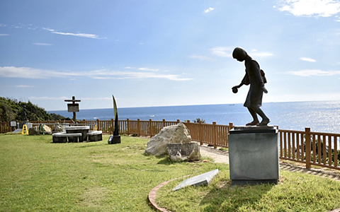 A statue standing in the Japanese Nursery Song Garden with a view of the ocean.