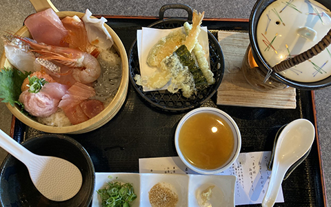 A bowl of sashimi, tempura, broth and a bowl for serving