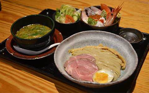 A bowl of boiled noodles with sliced pork and a boiled egg with a bowl of soup for dipping