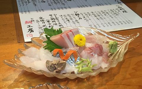 Glass dish filled with slices of fresh sashimi with a side of wasabi