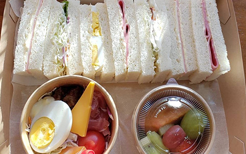 A box of egg and ham sandwiches with a fruit cup and salad