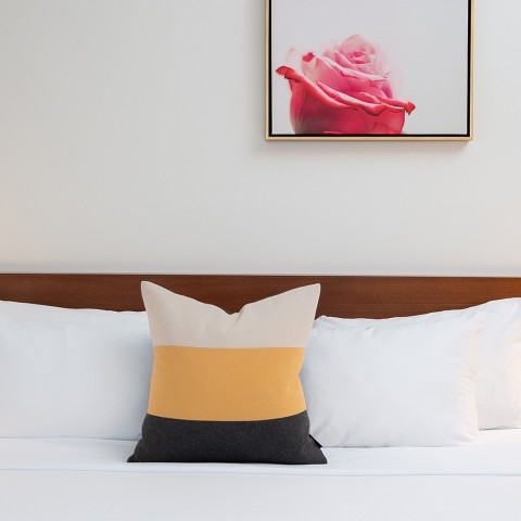 A large bed with cushion and a pink flower painting on the wall.