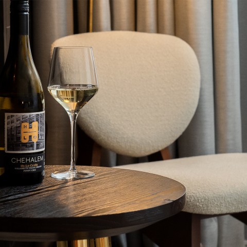 A wood table with a bottle of wine and a glass of wine and a chair behind it.