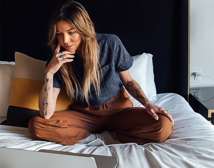 A woman sitting on a bed watching a laptop.