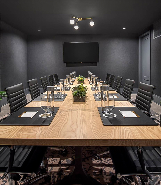 A meeting room with a large table, black chairs and a tv.