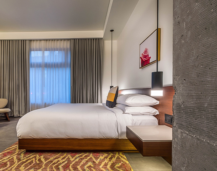 A room with a large bed, windows with curtains and an armchair