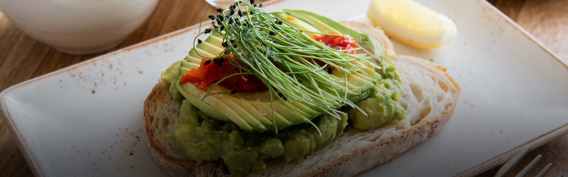 close up image of avocado toast with a lemon on a white plate