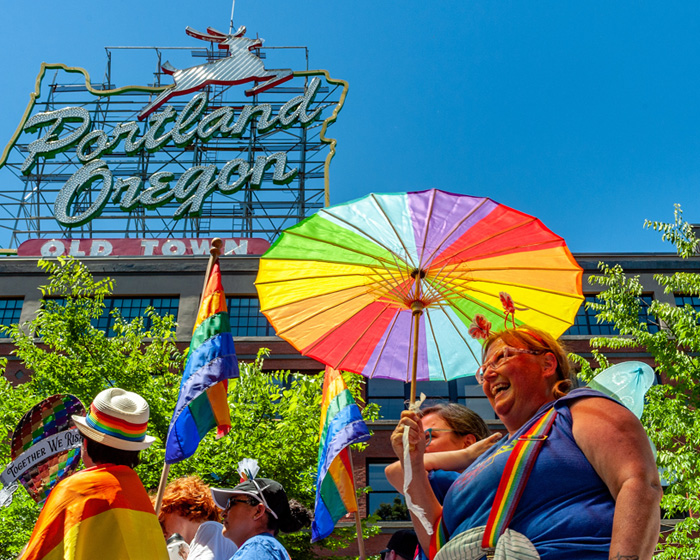 people in front of a portland orgeon sign with rainbow umbrella