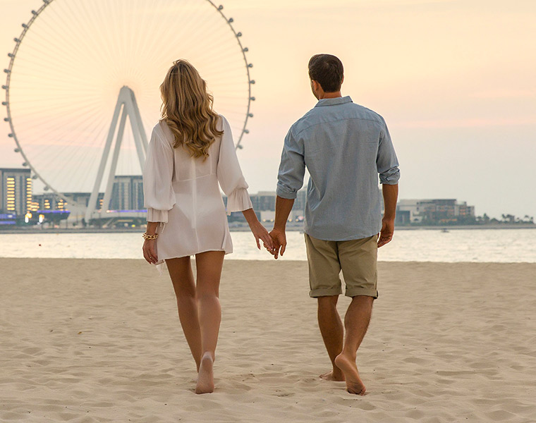 couple walking on the beach with the ferris wheel in the background