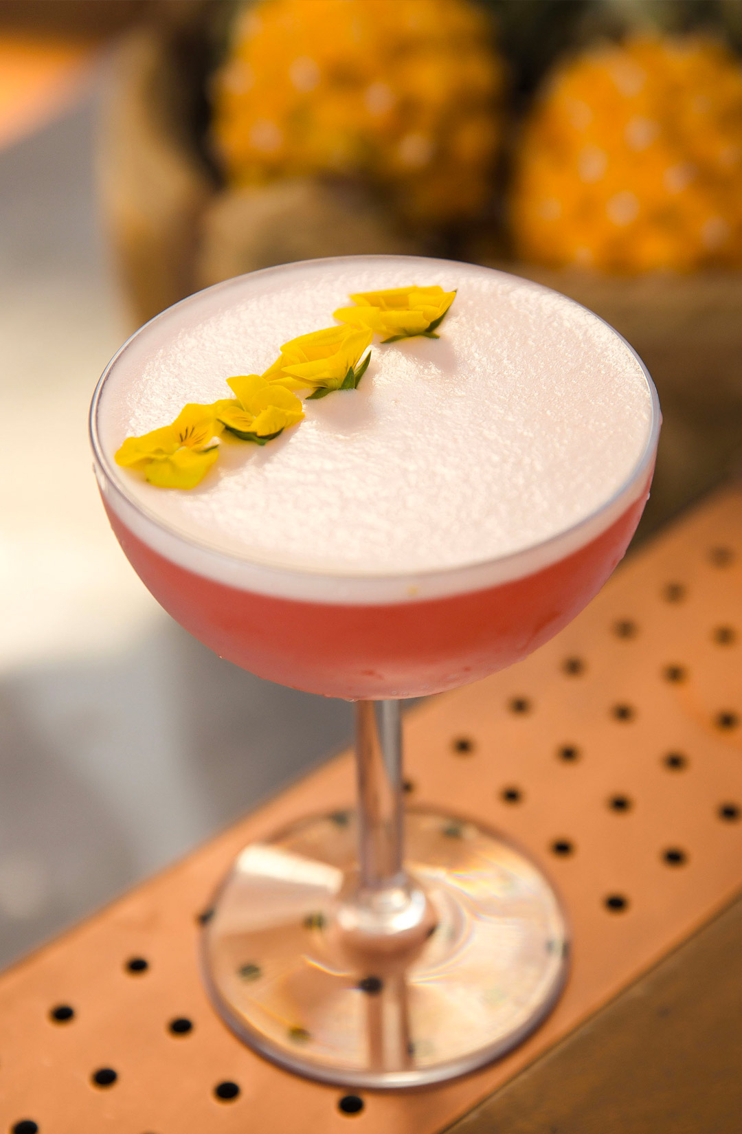 close up of a pink cocktail topped with small yellow flowers