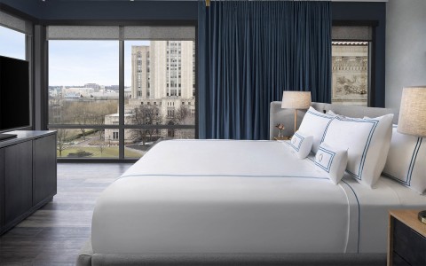 a large bed in a room with low lighting and a view of the city outside of the windows
