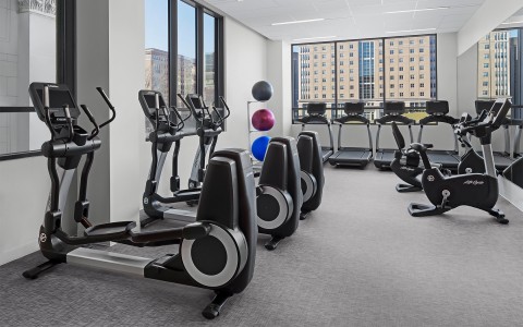 a workout room with machines and windows with sunlight coming in