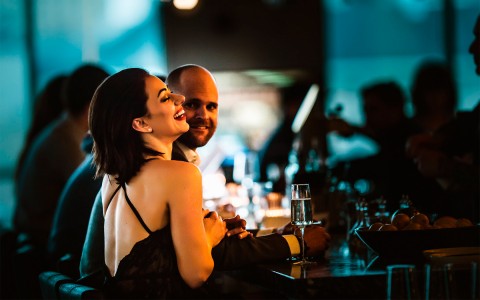 a man and woman sitting at a low lit bar