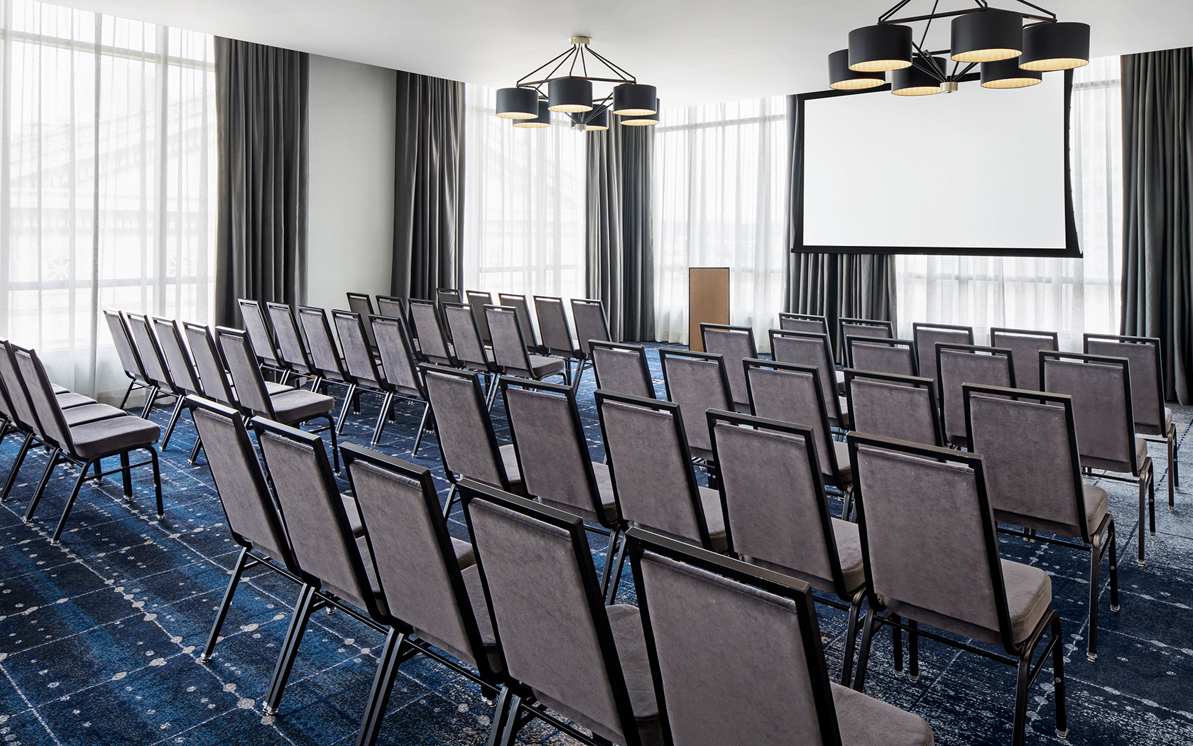 gallery many rows of chairs in a meeting room with a projection screen and dim lighting