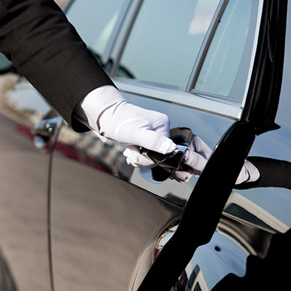a man wearing a suit and white gloves opening a car door