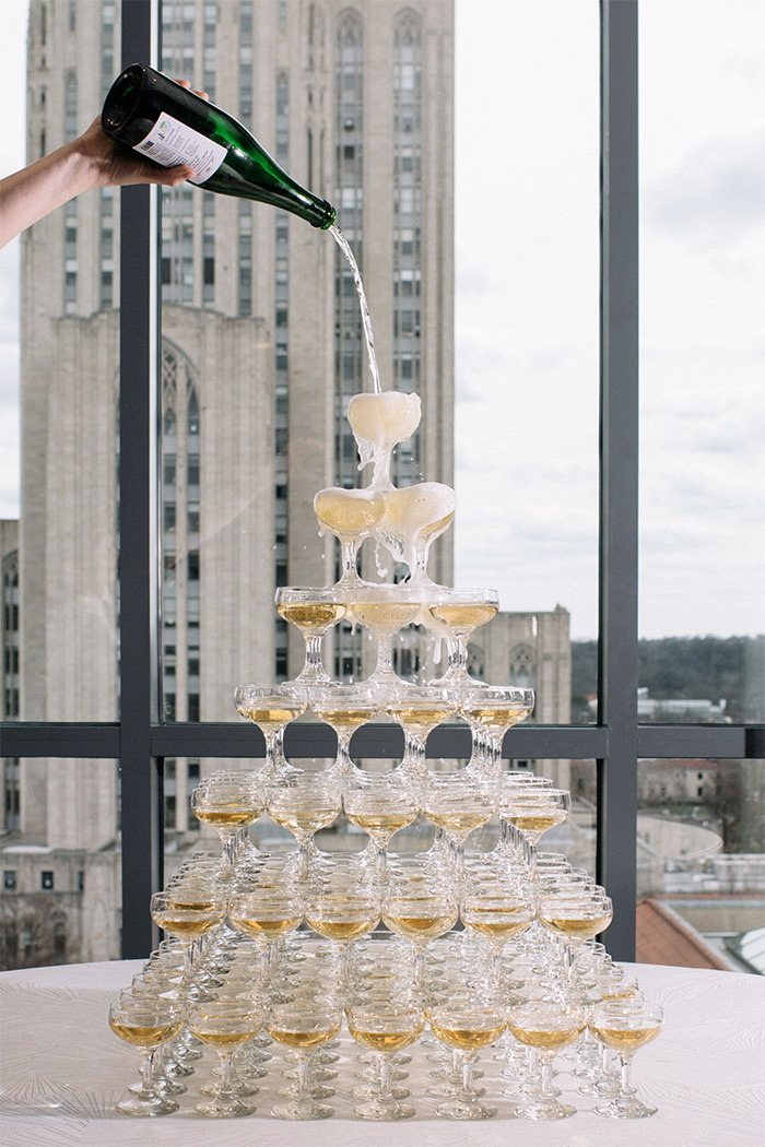 gallery a person pouring champagne into coupe glasses that are placed as a tower