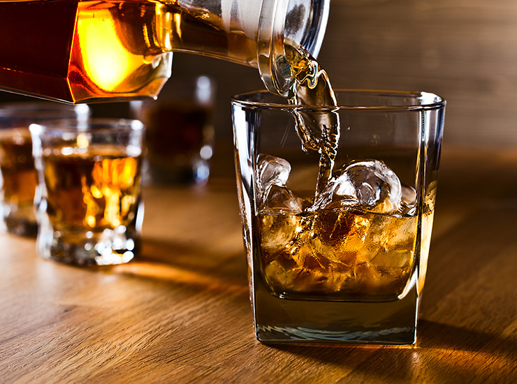 close up of a dark colored liquor being poured into a rocks glass