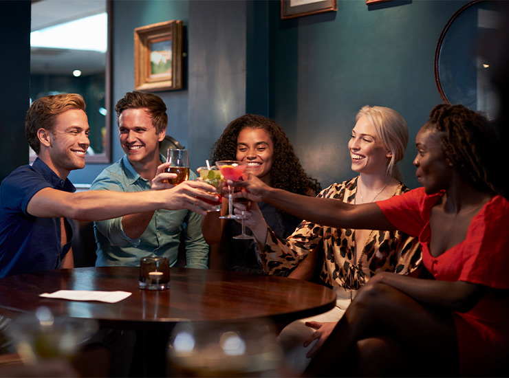 group of smiling friends clinking their drinks together in a restaurant