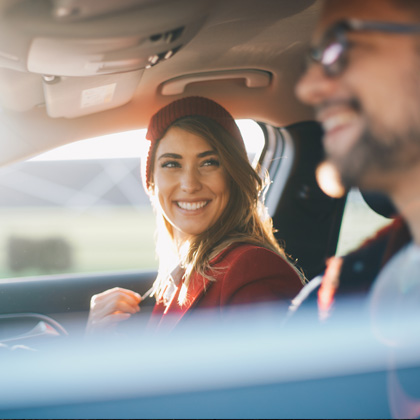 a smiling woman looking to her left at a man driving the car